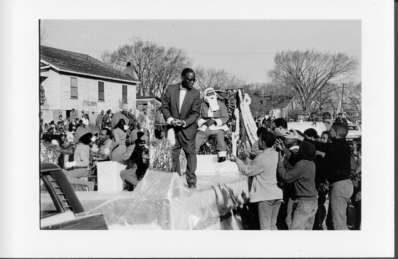 A parade with mostly African-American people watching and a float with a black man dressed as Santa Claus. 