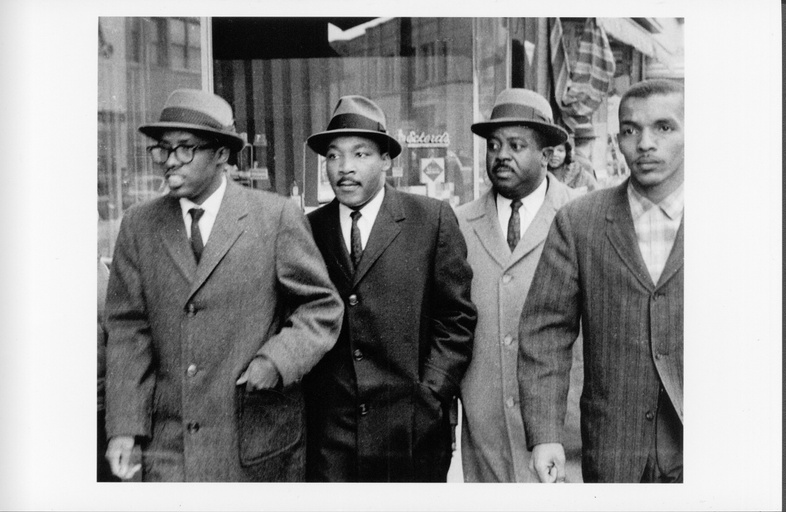 From left to right: Reverend Douglas Moore, Reverend Dr. Martin Luther King Jr., Reverend Ralph Abernathy, and an unidentified man walk outside in Durham.