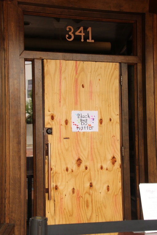 A small white piece of paper attached to a large board covering a window with the words "Black lives do matter."